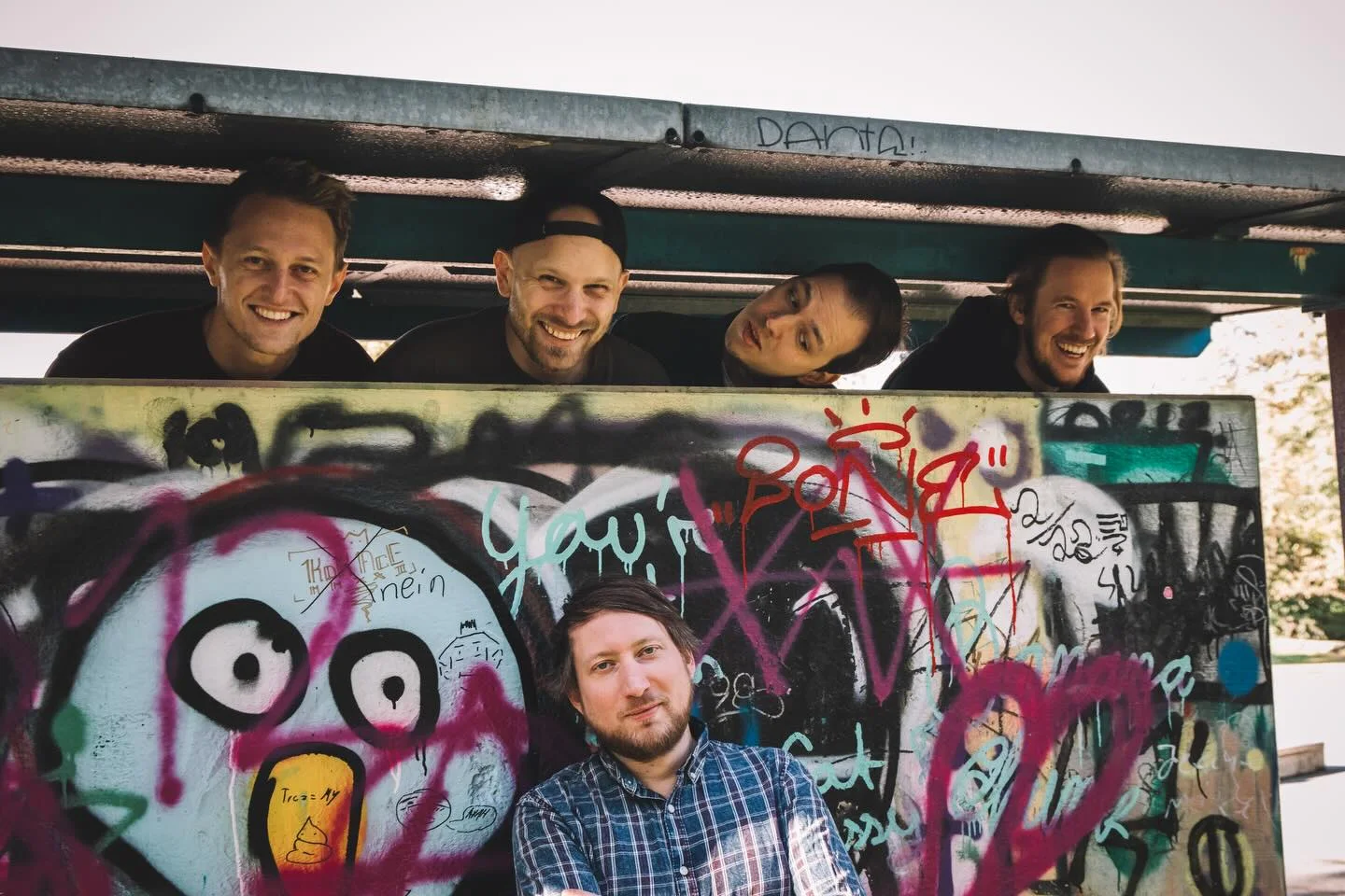 minor kings beim gemeinsamen Bandshooting vor einer mit Graffiti bemalten Tribüne